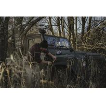 Mann befestigt etwas an einem Geländewagen im Gelände