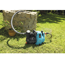 Gartenpumpe mit Schlauch auf Rasen vor Steinbrunnen