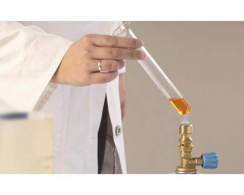 Ein Labormitarbeiter erhitzt eine Flüssigkeit im Reagenzglas mit einem Gasbrenner.