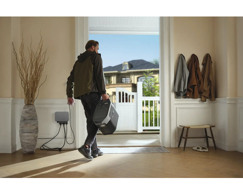 Person verlässt das Haus mit einer tragbaren Powerstation, die an eine Wandladestation angeschlossen ist