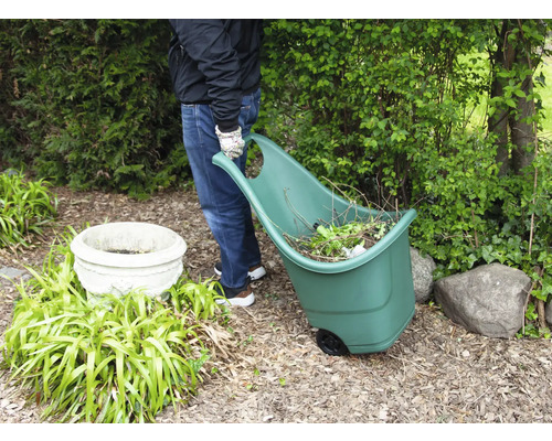 Eine Person zieht einen Gartenwagen mit Gartenabfällen durch einen Garten