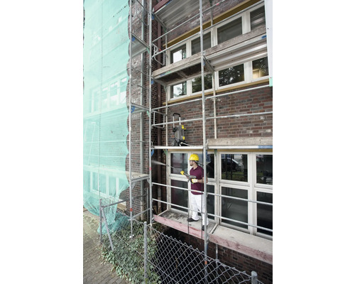 Mann auf Gerüst reinigt Fassade mit Hochdruckreiniger