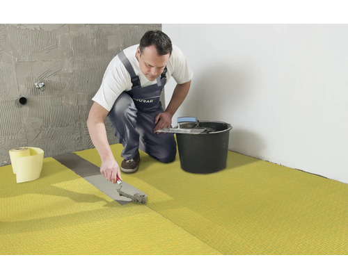 Handwerker verlegt Entkopplungsmatte im Badezimmer.