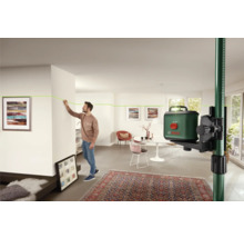 Raumszene mit einem Mann, der eine grüne Laserlinie mit einem Kreuzlinienlaser an einer Wand markiert