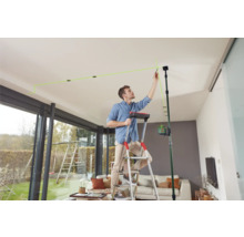 Mann auf einer Leiter, der mit einem Linienlaser Markierungen an der Decke anbringt.