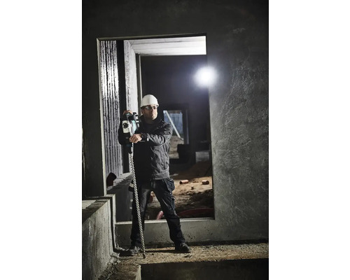 Bauarbeiter mit Schutzhelm und Schutzbrille hält eine Abbruchmaschine in einem Rohbau.