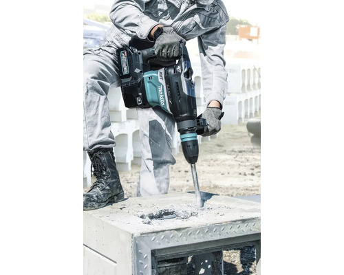 Ein Bauarbeiter benutzt einen Akku-Bohrhammer der Marke Makita, um ein Loch in einen Betonblock zu bohren.