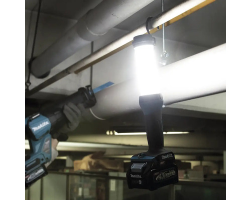 Makita Akku-Lampe an einer Rohrleitung hängend, eine Säbelsäge im Hintergrund