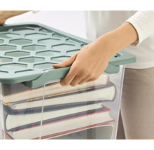 Person verschließt eine gefüllte, durchsichtige Aufbewahrungsbox mit Deckel