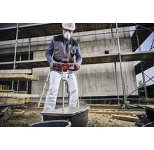 Ein Bauarbeiter mischt mit einem elektrischen Mörtelrührer Mörtel in einer Wanne auf einer Baustelle.