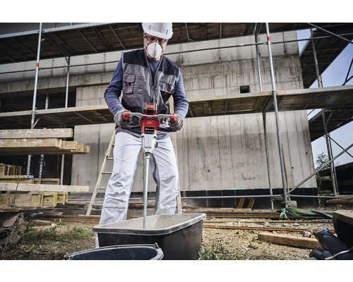Ein Bauarbeiter mischt mit einem elektrischen Mörtelrührer Mörtel in einer Wanne auf einer Baustelle.