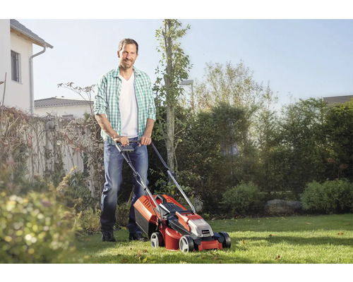 Mann mäht Rasen mit einem Akku-Rasenmäher im Garten.