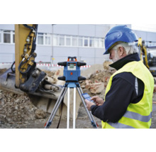 Bauarbeiter mit Rotationslaser auf der Baustelle mit Bagger im Hintergrund