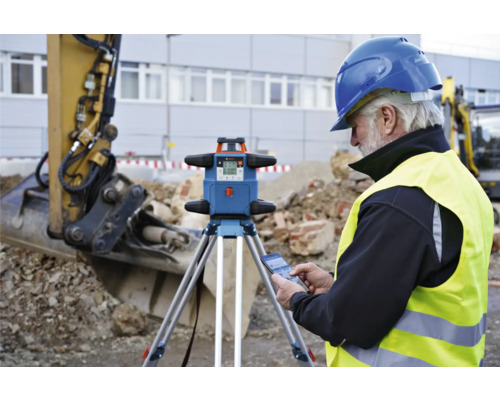 Bauarbeiter mit Rotationslaser auf der Baustelle mit Bagger im Hintergrund