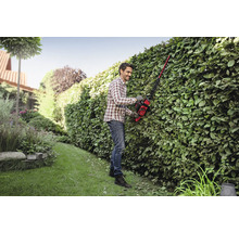 Ein Mann beschneidet mit einer Heckenschere eine Hecke in einem Garten.