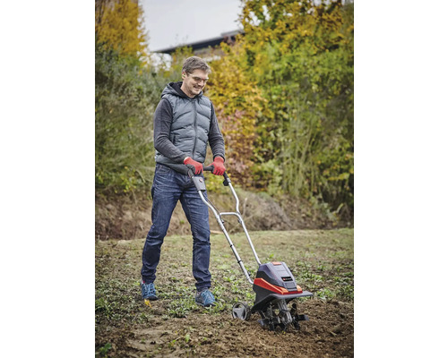 Mann arbeitet mit einer Gartenfräse zur Bodenbearbeitung im Garten.