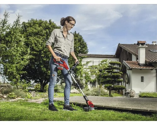 Frau verwendet einen Akku-Rasentrimmer im Garten für Rasenpflege