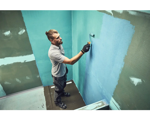 Mann streicht eine Wand mit einer Farbrolle in einem Badezimmer