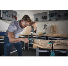Mann bohrt mit einer Bohrmaschine Dübellöcher in ein Holzbrett auf einer Werkbank.