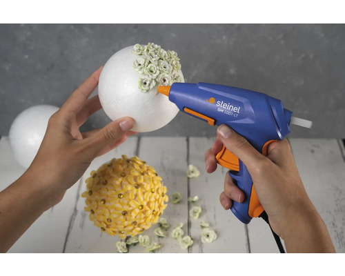 Person verwendet eine Heißklebepistole, um Dekorationen auf einer Styroporkugel anzubringen