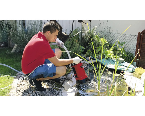 Mann benutzt eine Teichpumpe zum Entleeren eines Gartenteichs.