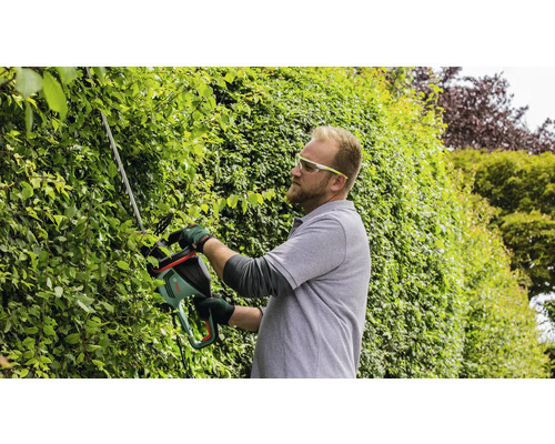 Mann schneidet Hecke mit einer Heckenschere.