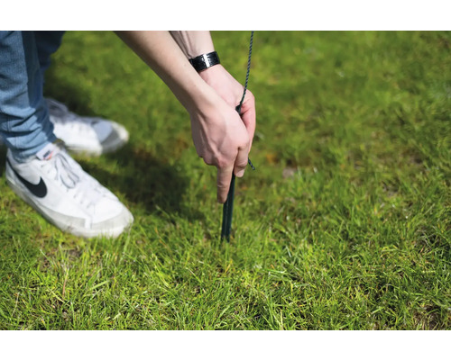 Person befestigt einen Hering im Gras