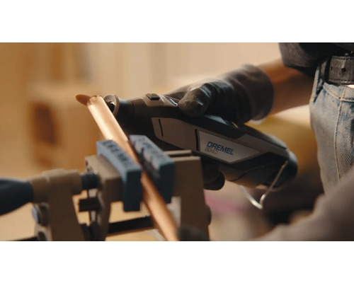 Eine Person benutzt ein Dremel 8240 Multifunktionswerkzeug, um ein Kupferrohr zu schneiden, das in einem Schraubstock befestigt ist.