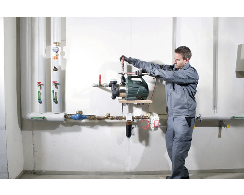 Installation einer Gartenpumpe durch einen Handwerker an einer Wand mit Rohren.