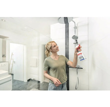 Frau reinigt mit Schimmelentferner eine Dusche im hellen Badezimmer.