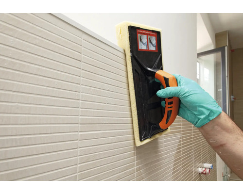 Fliesenleger reinigt eine geflieste Wand mit einem Fliesenschwammbrett