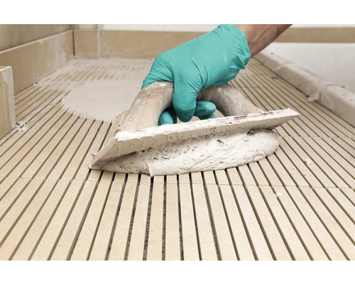 Handwerker mit Gummihandschuhen und Spachtel beim Verfugen von Fliesen