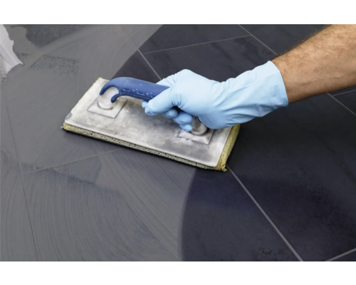 Hand mit Schutzhandschuh verwendet ein Fugbrett auf Fliesen.