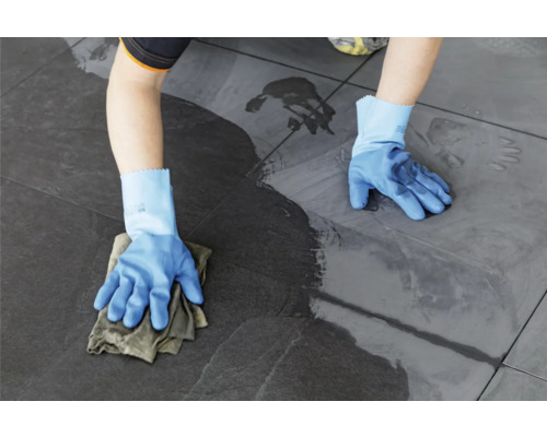 Eine Person reinigt Bodenfliesen mit einem Tuch und Handschuhen