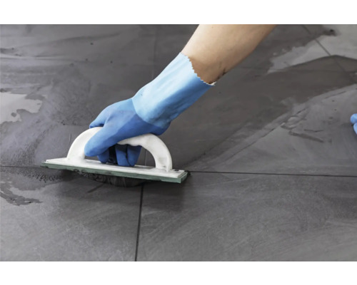 Eine Person verfugt Fliesen mit einem Fugenbrett.