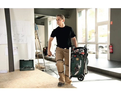 Ein Mann transportiert eine Metabo Tischkreissäge im zusammengeklappten Zustand.