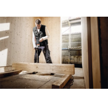 Handwerker bohrt mit einer Bohrmaschine in ein Holzbrett in einem Raum mit Holzpaneelen.