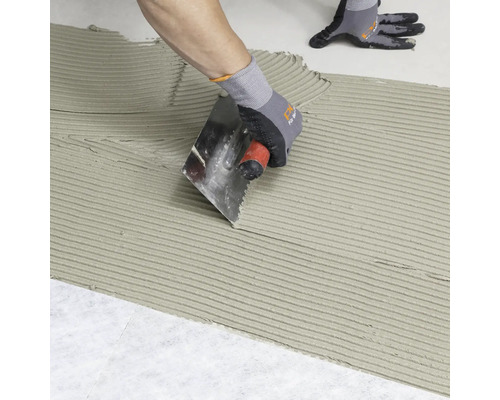 Fliesenleger trägt mit einer Kelle Fliesenkleber auf einen Untergrund auf