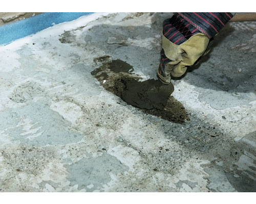 Eine mit einem Handschuh geschützte Hand trägt Spachtelmasse auf eine Betonoberfläche auf.