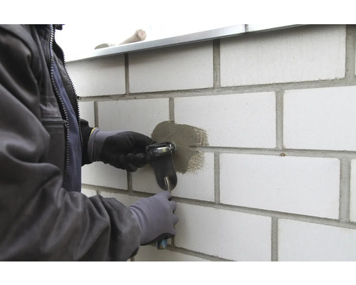 Handwerker mit Fugenpistole beim Verfugen einer Mauer.