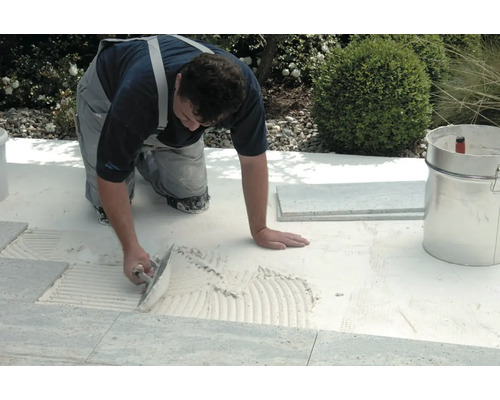 Handwerker verlegt Fliesen im Außenbereich mit einer Glättkelle und Fliesenkleber.