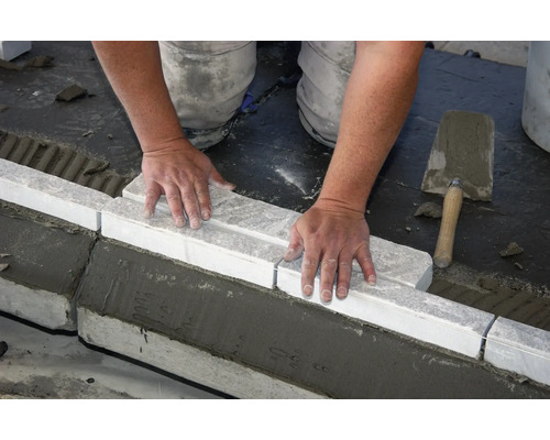 Handwerker verlegt Bordsteine mit Mörtel und Kelle