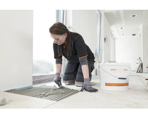 Frau verlegt Fliesen mit Fliesenkleber der Marke PCI