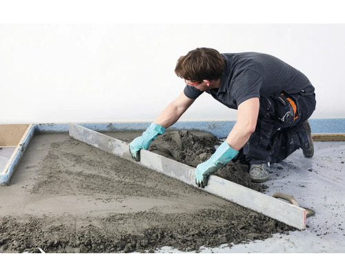 Handwerker zieht Estrich mit einer Abziehstange ab.