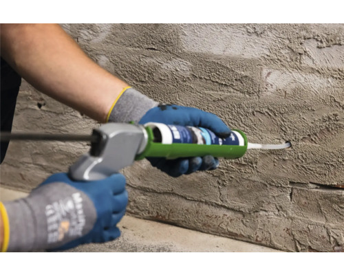 Person verwendet eine Kartuschenpistole an einer Wand, um eine Fuge zu versiegeln.