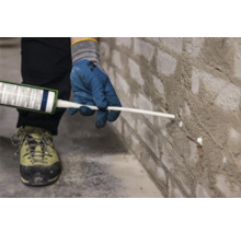Eine Person dichtet eine Ziegelwand mit Dichtmasse ab.