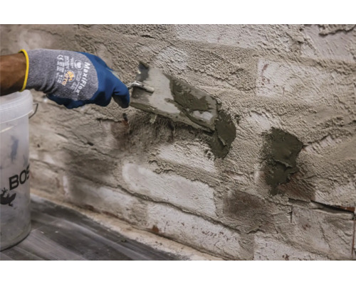 Handwerker verfugt eine Backsteinwand mit einer Spachtel und Fugenmörtel