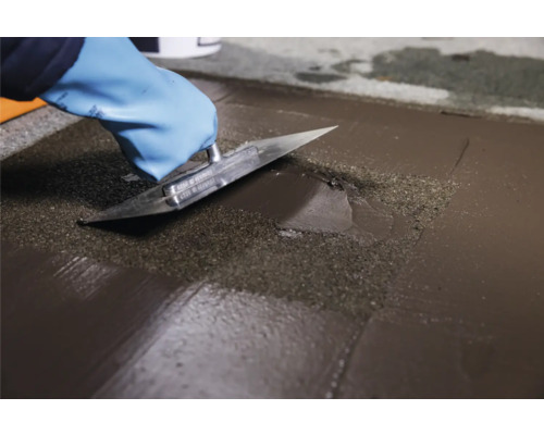 Handwerker glättet Bodenausgleichsmasse mit einer Glättkelle