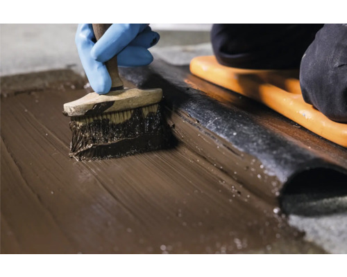 Aufbringen von Dichtmasse auf Dachpappe mit einem Pinsel.