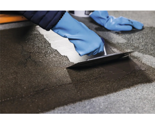 Auftragen von Bitumen Dachlack mit einer Glättkelle durch eine Person mit Handschuhen.